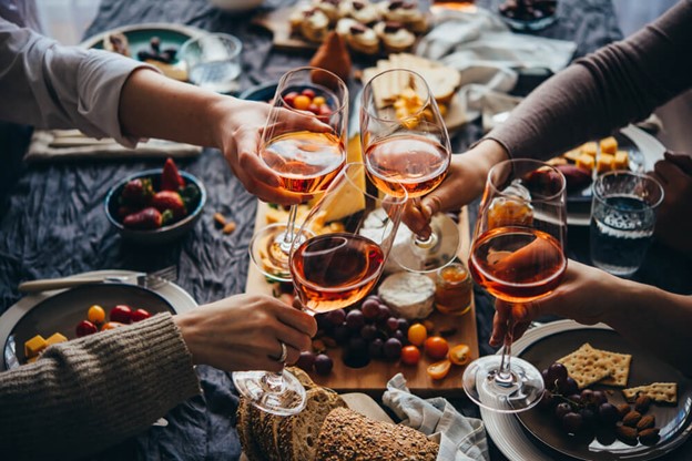 Hands toasting with wine glasses over cheese board