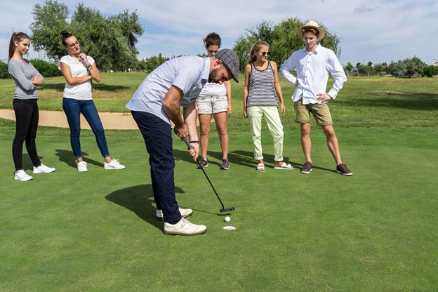man putting a golf ball on green while friends watch